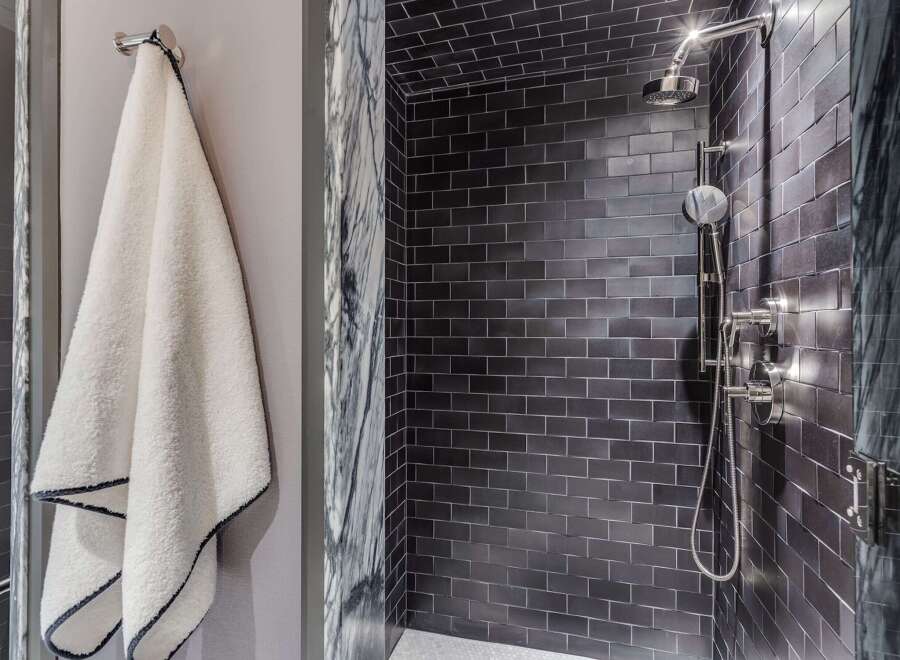 Experience modern luxury in this stunning bathroom featuring a sleek, dark tiled shower with a rainfall showerhead and elegant chrome fixtures.