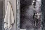 Experience modern luxury in this stunning bathroom featuring a sleek, dark tiled shower with a rainfall showerhead and elegant chrome fixtures.