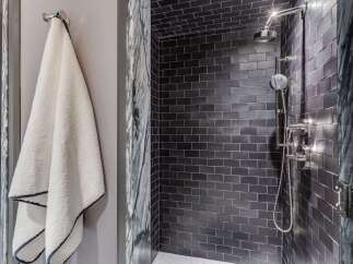 Experience modern luxury in this stunning bathroom featuring a sleek, dark tiled shower with a rainfall showerhead and elegant chrome fixtures.