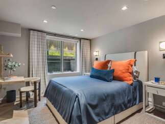 This modern bedroom features a comfortable queen-size bed with a navy blue duvet and vibrant orange accent pillows, creating a cozy and stylish retreat.