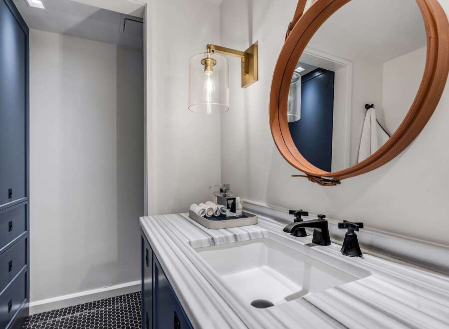 This modern bathroom features a sleek white undermount sink set into a stunning marble countertop with dark blue cabinetry below.