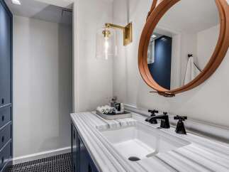 This modern bathroom features a sleek white undermount sink set into a stunning marble countertop with dark blue cabinetry below.