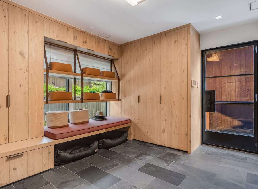 Discover this beautifully designed mudroom featuring custom light wood cabinetry for ample storage and a built-in bench with a comfortable cushion.
