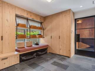 Discover this beautifully designed mudroom featuring custom light wood cabinetry for ample storage and a built-in bench with a comfortable cushion.