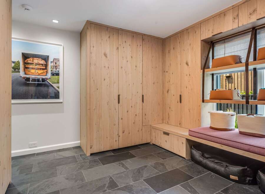 This modern entryway features a custom built-in wood cabinet system with ample storage and a comfortable bench seating area.