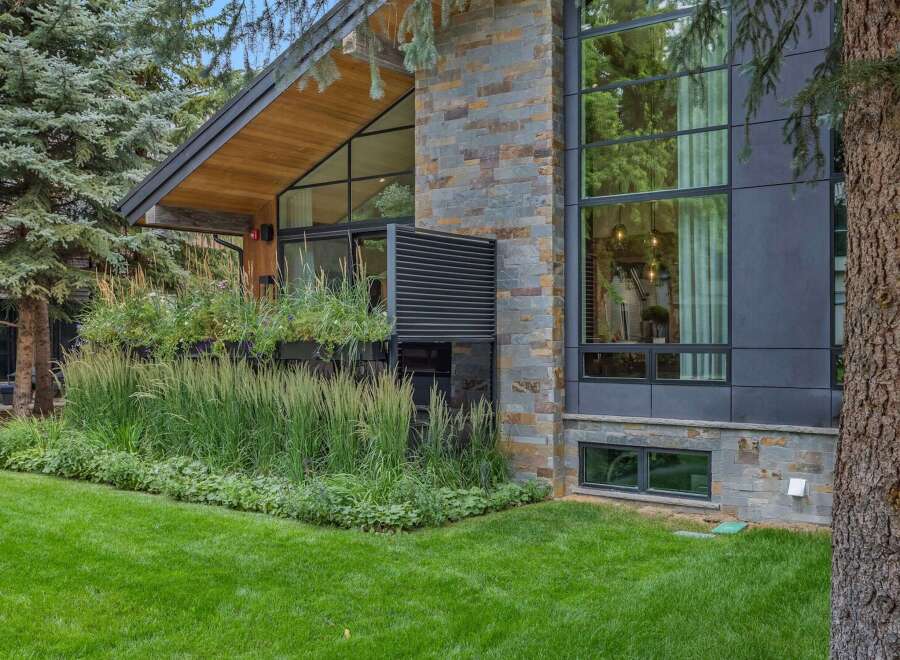 Experience modern luxury in this stunning home, featuring a striking facade of natural stone and dark metal paneling.