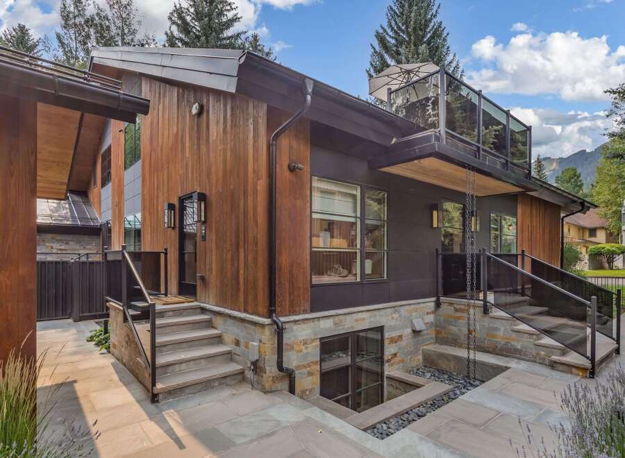 Experience modern luxury in this stunning home featuring a striking blend of natural wood and dark metal siding.