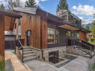 Experience modern luxury in this stunning home featuring a striking blend of natural wood and dark metal siding.