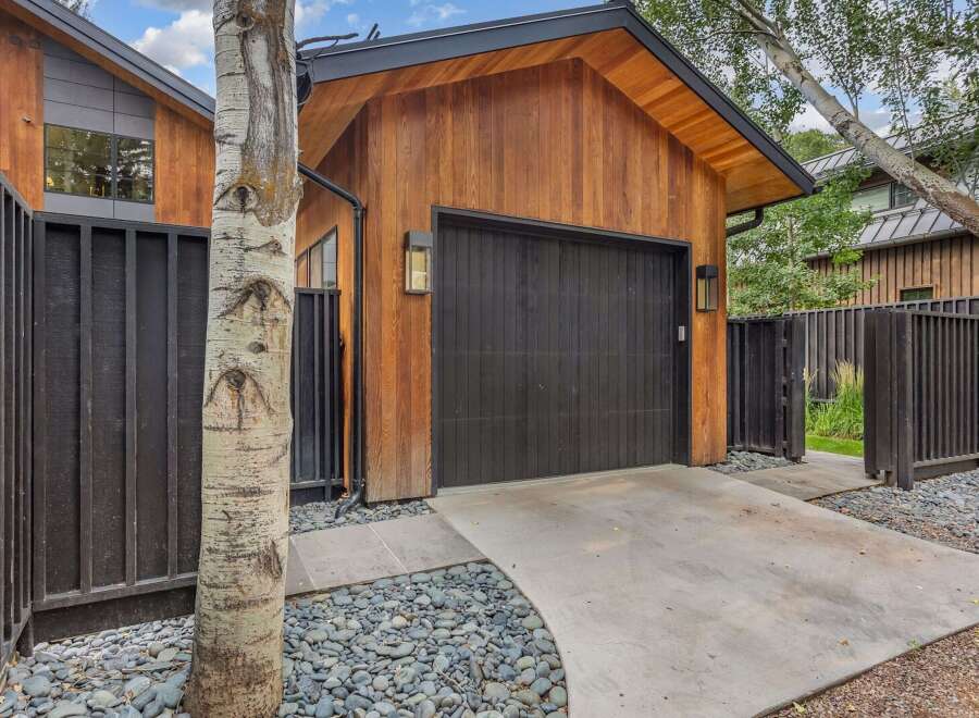 This modern garage features a striking vertical wood-paneled exterior complemented by a sleek black garage door and matching fence.