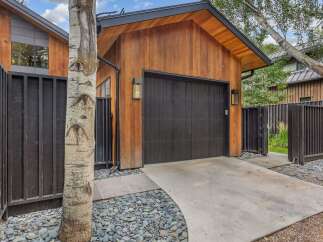 This modern garage features a striking vertical wood-paneled exterior complemented by a sleek black garage door and matching fence.
