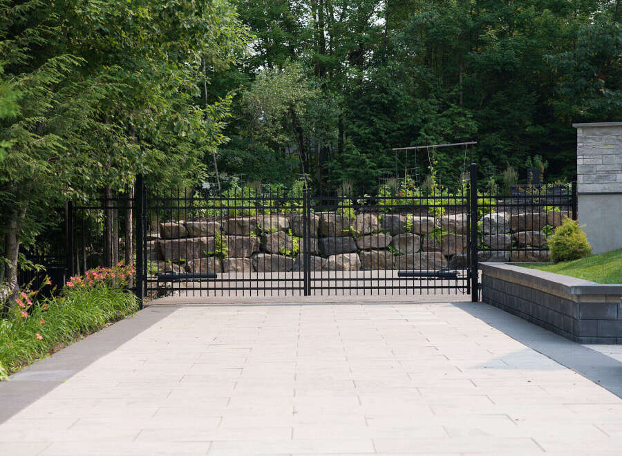 Experience unparalleled privacy and security with this elegant black metal estate gate, set against a backdrop of lush greenery and natural stone landscaping.
