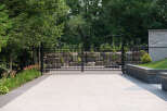 Experience unparalleled privacy and security with this elegant black metal estate gate, set against a backdrop of lush greenery and natural stone landscaping.