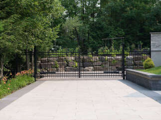 Experience unparalleled privacy and security with this elegant black metal estate gate, set against a backdrop of lush greenery and natural stone landscaping.