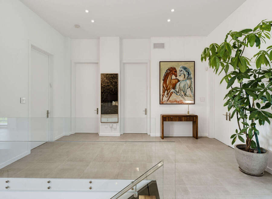 This spacious hallway features a modern design with sleek glass railings and neutral-toned tiled flooring.