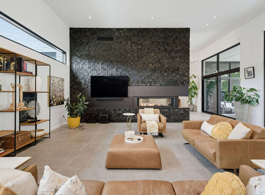 Experience modern luxury in this spacious living room, featuring a striking black stone accent wall with a sleek fireplace and integrated television.