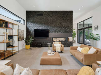 Experience modern luxury in this spacious living room, featuring a striking black stone accent wall with a sleek fireplace and integrated television.