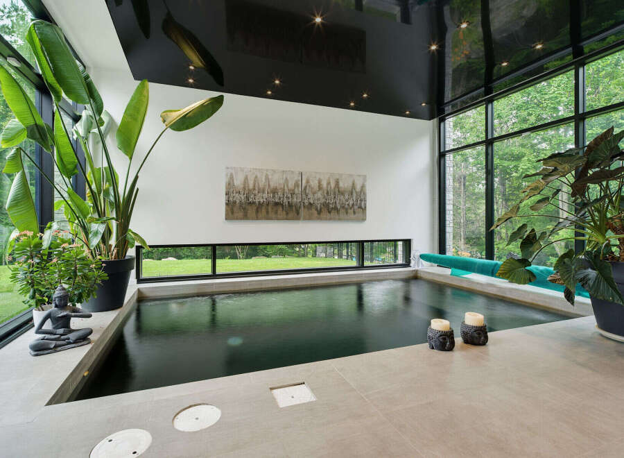 Experience ultimate relaxation in this indoor oasis, featuring a sleek, dark-water pool surrounded by lush greenery and expansive windows.