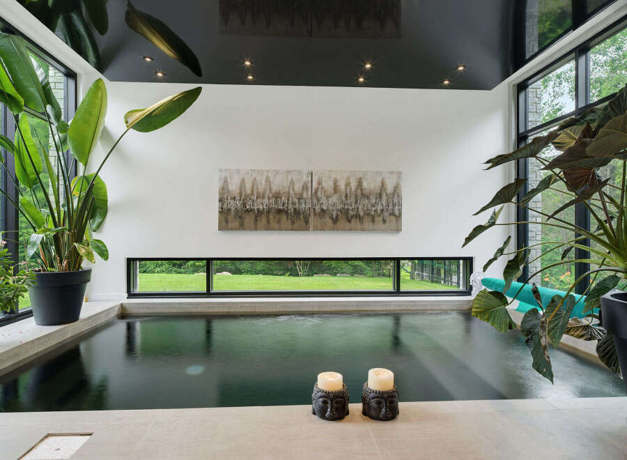 Experience ultimate relaxation in this indoor oasis, featuring a sleek, dark-water pool surrounded by lush greenery and expansive windows.