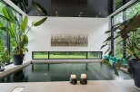 Experience ultimate relaxation in this indoor oasis, featuring a sleek, dark-water pool surrounded by lush greenery and expansive windows.