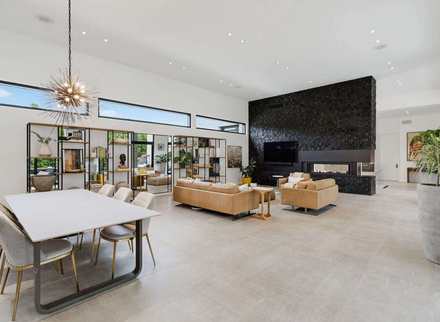 Experience modern luxury in this expansive open-concept living and dining area, featuring a striking black stone fireplace and a unique sputnik chandelier.