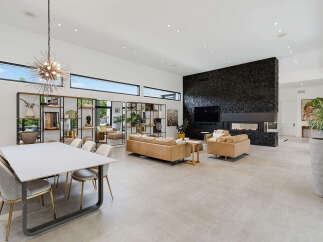 Experience modern luxury in this expansive open-concept living and dining area, featuring a striking black stone fireplace and a unique sputnik chandelier.