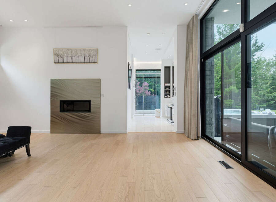 Experience modern luxury in this stunning living space featuring a sleek fireplace and expansive floor-to-ceiling windows that offer breathtaking views of the lush backyard.
