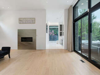 Experience modern luxury in this stunning living space featuring a sleek fireplace and expansive floor-to-ceiling windows that offer breathtaking views of the lush backyard.