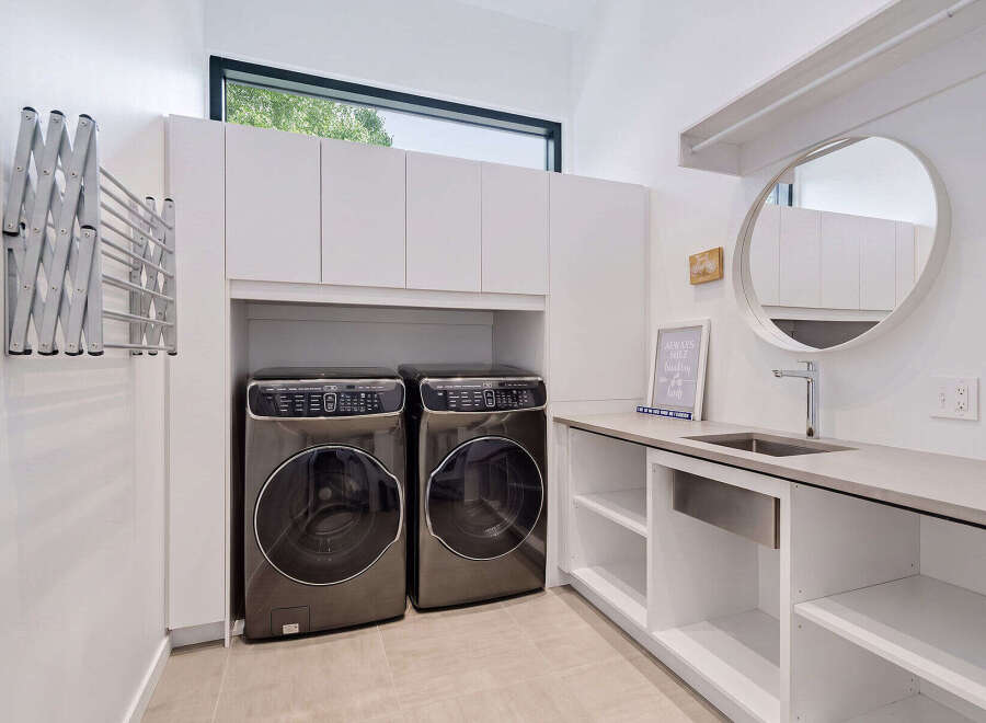 This modern laundry room features two sleek, front-loading washing machines and dryers, complemented by ample white cabinetry for storage.
