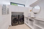 This modern laundry room features two sleek, front-loading washing machines and dryers, complemented by ample white cabinetry for storage.