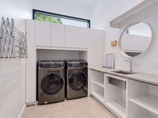 This modern laundry room features two sleek, front-loading washing machines and dryers, complemented by ample white cabinetry for storage.