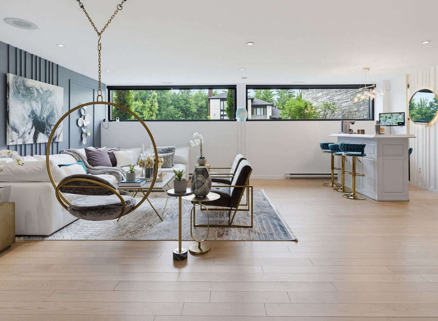 Experience modern living in this spacious open-concept living area, featuring a stylish white bar with plush blue stools and a unique hanging chair.