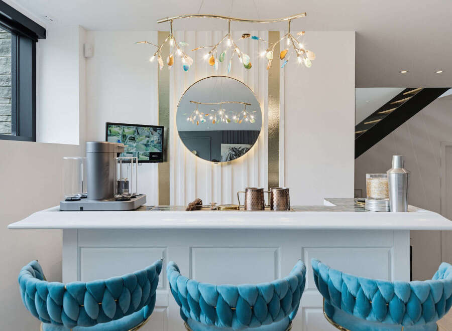 Experience luxury and entertainment in this stunning home bar area, featuring plush velvet bar stools and a sleek white countertop perfect for hosting.