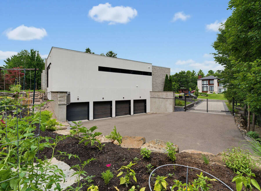 Discover this modern architectural marvel featuring a sleek white facade and multiple garage doors, complemented by a lush garden in the foreground.