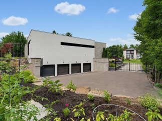 Discover this modern architectural marvel featuring a sleek white facade and multiple garage doors, complemented by a lush garden in the foreground.