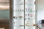 Showcasing a modern kitchen with a sleek, illuminated glass display cabinet filled with elegant glassware and decorative items.