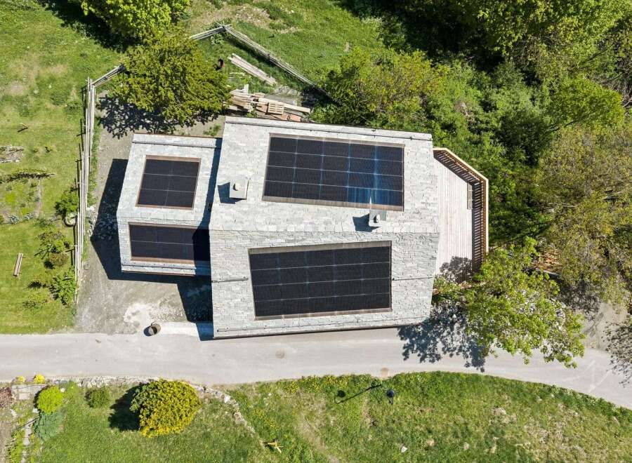 Experience sustainable living in this modern home featuring a sleek stone facade and an expansive rooftop solar panel system.