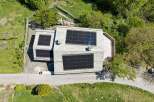 Experience sustainable living in this modern home featuring a sleek stone facade and an expansive rooftop solar panel system.