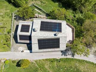 Experience sustainable living in this modern home featuring a sleek stone facade and an expansive rooftop solar panel system.
