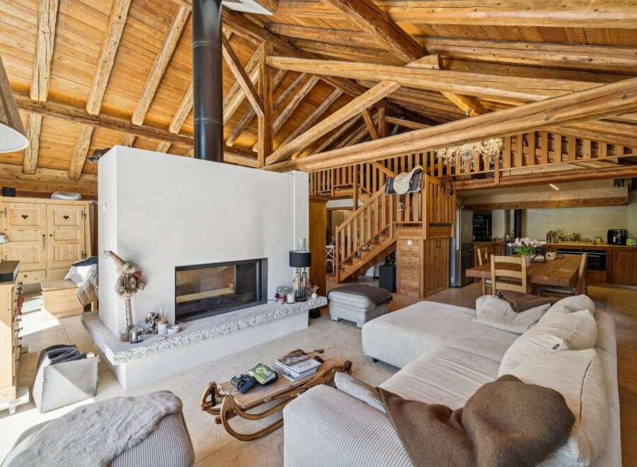 Experience rustic charm in this spacious living area, featuring a striking white fireplace as the focal point and exposed wooden beams overhead.
