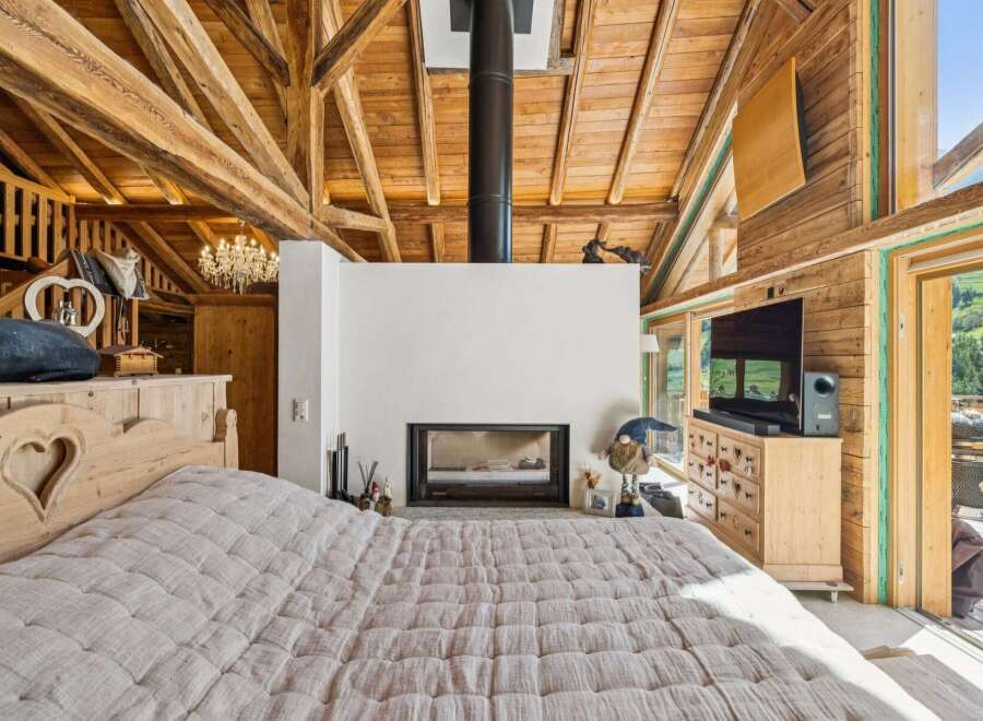 Experience rustic charm and modern comfort in this stunning bedroom featuring a cozy fireplace and a luxurious wooden-beamed ceiling.