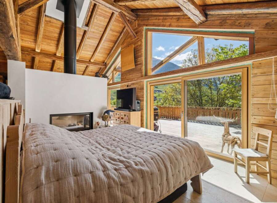 Experience rustic luxury in this stunning mountain retreat, featuring a cozy bedroom with a modern fireplace and a large, open-concept living space.