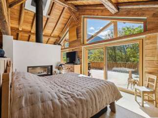 Experience rustic luxury in this stunning mountain retreat, featuring a cozy bedroom with a modern fireplace and a large, open-concept living space.