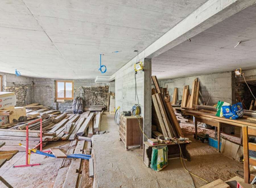 This unfinished concrete space offers a blank canvas for renovation, featuring exposed stone walls and wooden beams.