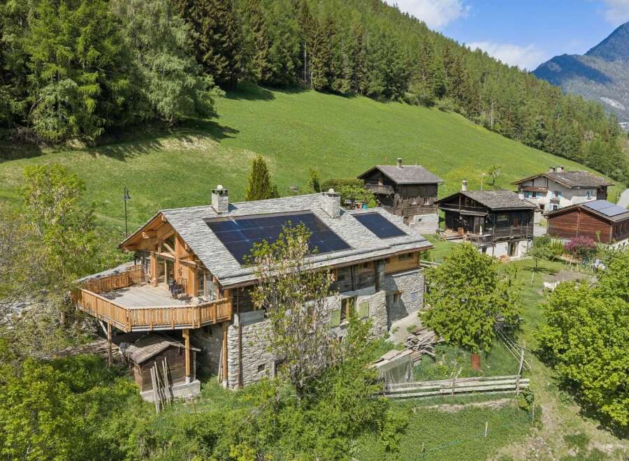 Experience sustainable living in this charming alpine home, featuring a modern roof with solar panels and a spacious wooden deck perfect for enjoying the mountain views.