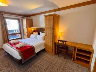 Experience cozy mountain living in this charming hotel room, featuring a comfortable queen-size bed adorned with plush white linens and a striking red runner.