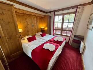 Experience cozy mountain living in this charming hotel room, featuring two comfortable beds adorned with plush red throws and white robes.