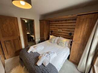 Experience rustic charm in this cozy bedroom featuring a comfortable bed adorned with decorative pillows and plush white towels.