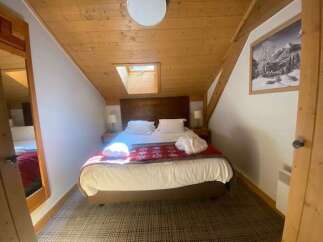 Experience cozy mountain living in this charming attic bedroom, featuring a comfortable queen-size bed adorned with a festive red throw and plush white linens.