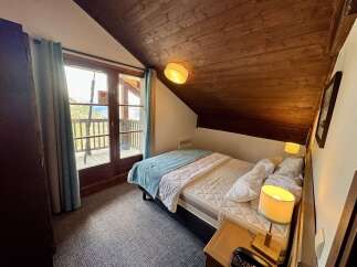 Experience cozy mountain living in this charming attic bedroom, featuring a comfortable bed adorned with a soft teal throw and crisp white linens.