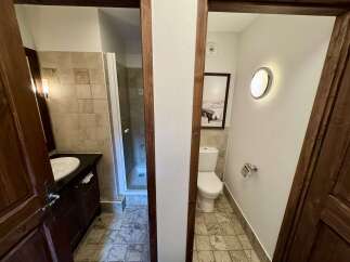 Discover this charming bathroom featuring a modern vanity with ample storage and a sleek sink, complemented by a separate toilet area with a stylish wall-mounted light fixture.